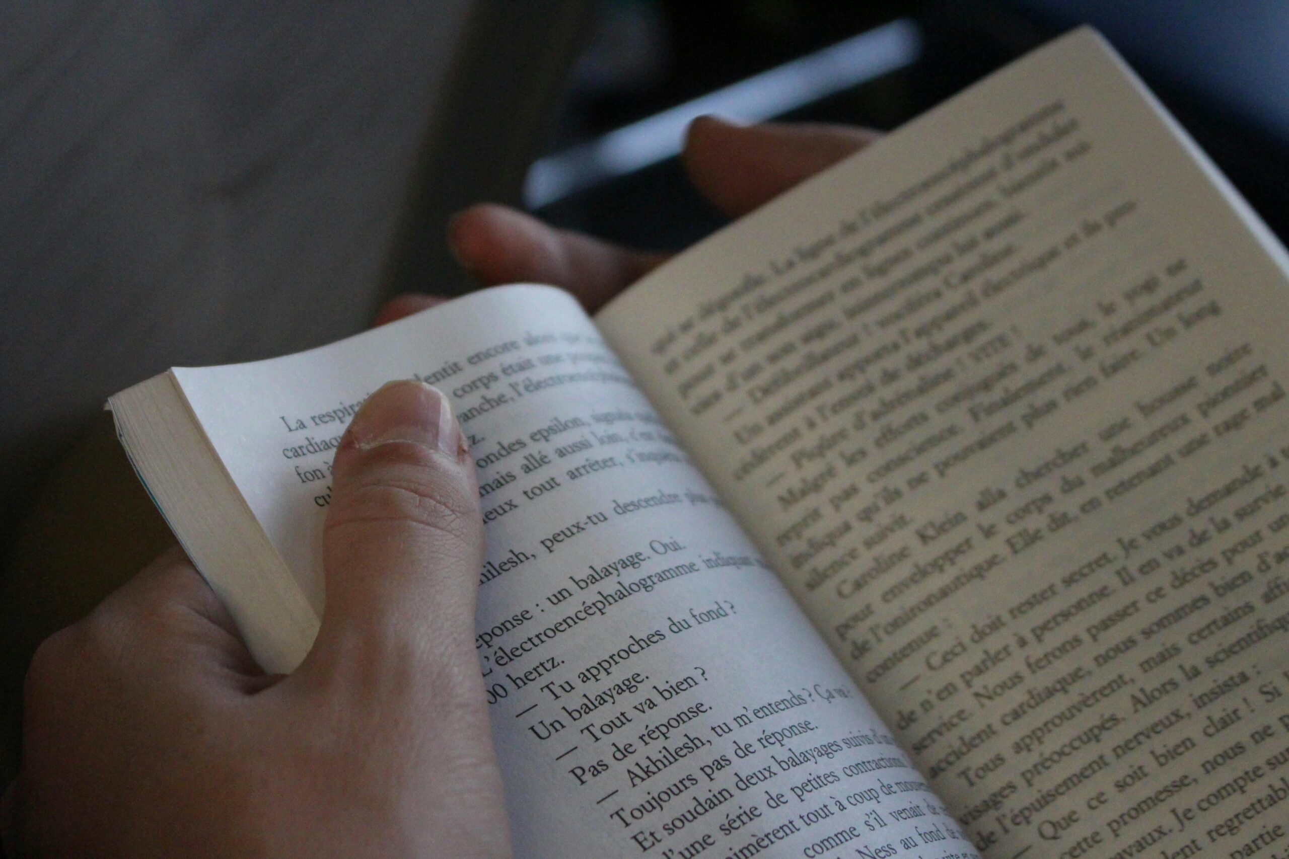 A person reading a book, focusing on the text and hands, in a cozy indoor setting.